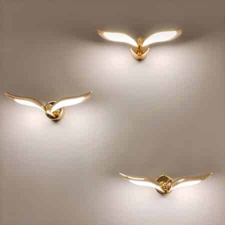 Gray wall with 3 staggered wall sconces in the shape of a golden bird with light on the underside of the wings.