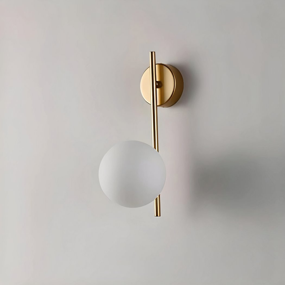 Golden wall light with straight stem and globe hanging over an armchair and plant