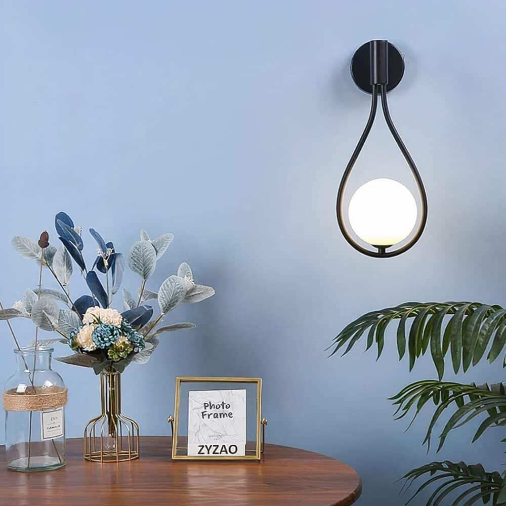 A black teardrop-shaped wall light with a ball bulb hangs on a blue wall in a living room.