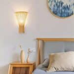 a bohemian-style bamboo wall lamp is seen on a white wall in a bedroom