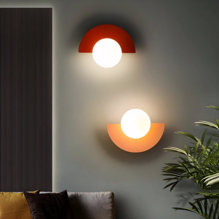 Two retro-style half-moon wall sconces in red and pink hang on a wall next to a house plant