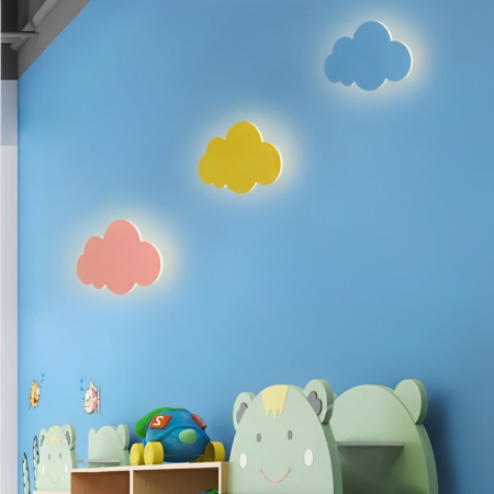 There are three cloud-shaped wall lights: one blue, one pink and one yellow, hanging on a blue wall in a child's bedroom