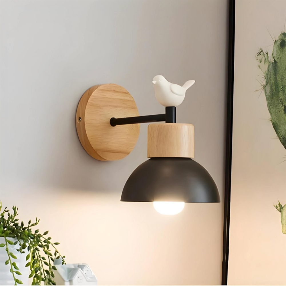Modern black wall lamp in wood with a bird that is lit, next to a picture and a fake plant