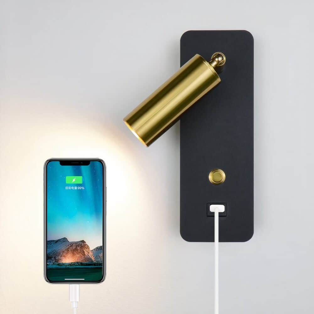 Adjustable wall light with black base and gold head, gold switch and USB socket. A smartphone lit next to it and connected with a white cable to the wall light.