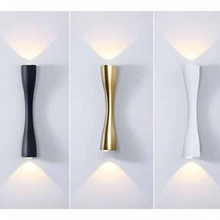 Three lit wall sconces: one black, one white and one gold, hung on a wall