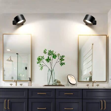 2 round black wall sconces light up a vintage black bathroom cabinet with gold handles, green plant on top, mirror on square base. Under each sconce is a large rectangular mirror.