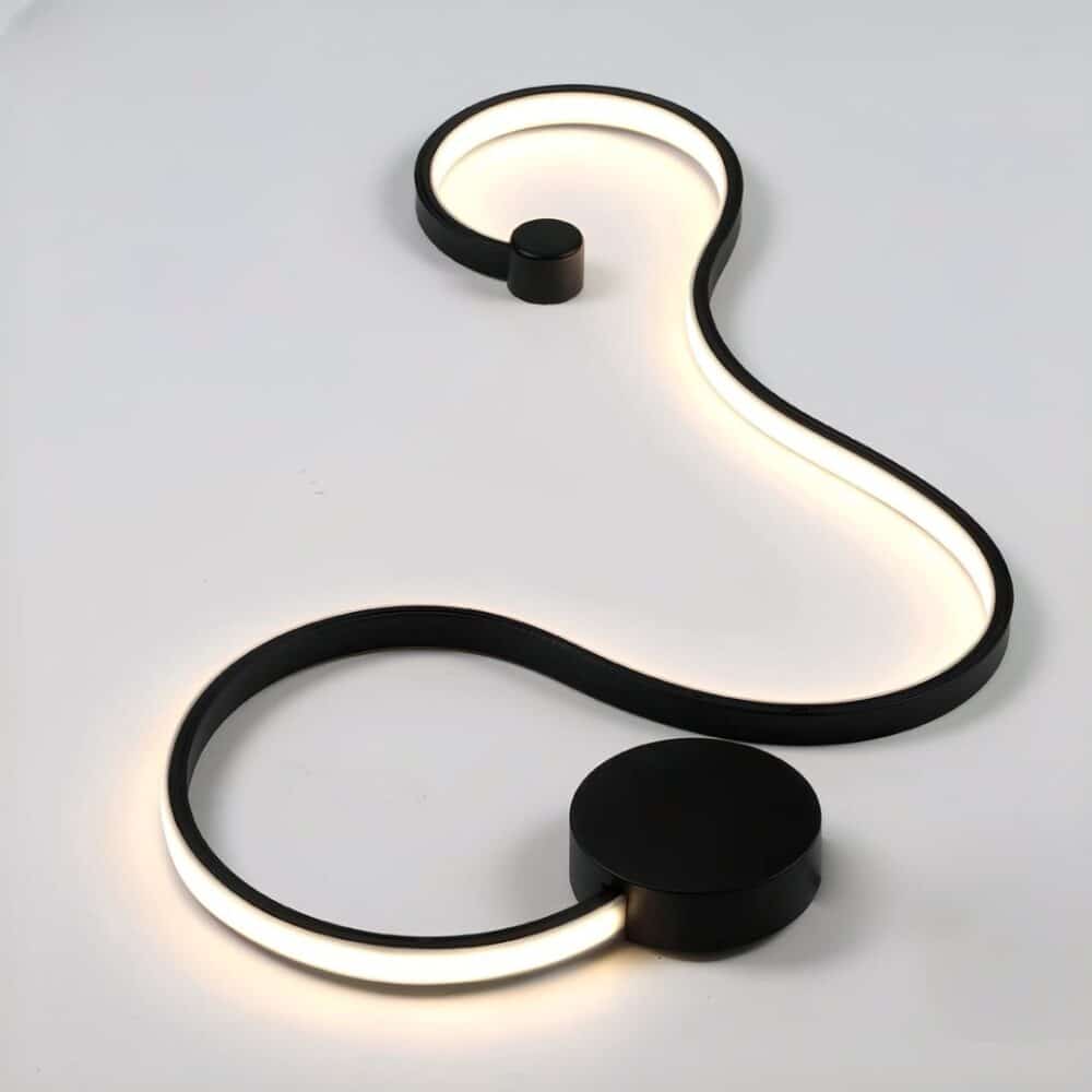 Black wall light in the form of a luminous ribbon on a white base. A black circle at the bottom and a smaller one at the other end.