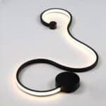 Black wall light in the form of a luminous ribbon on a white base. A black circle at the bottom and a smaller one at the other end.