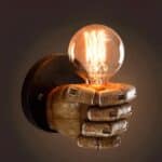 Wall light imitating a left wooden hand holding a light bulb. On brown background.