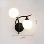 Black metal wall light with 2 luminous balls, one on the vertical stem and the other under the horizontal stem on the right. Mounted on a grey wall. Dimensions are shown on the left and bottom of the sconce.