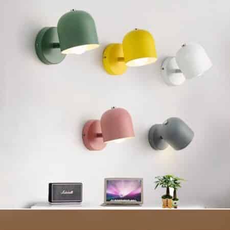 on a light gray wall are several scandinavian-style wall sconces in different colors, pink green gray yellow and white