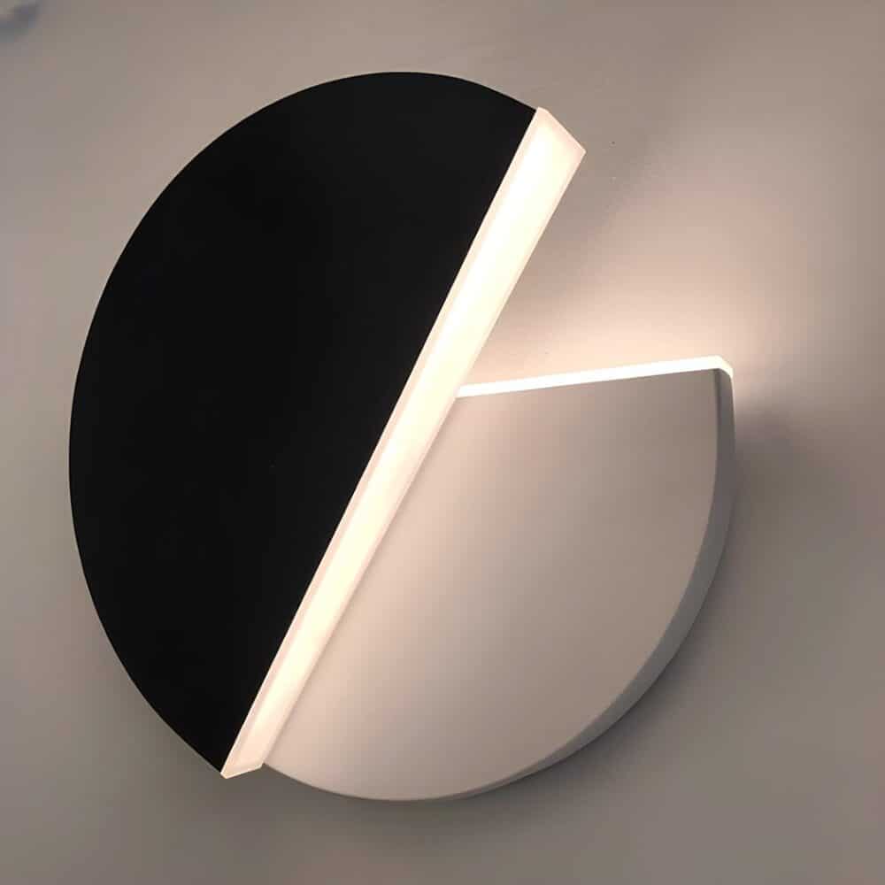 Wall light in 2 half-moon parts, one of which is black and rotatable. The other fixed part is white. Light is diffused by the edges of the half-moons. The rotating part is open at approximately 45 degrees.