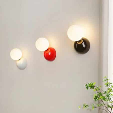 on a light gray wall, we see 3 ball-shaped wall sconces for headboards in three different colors, one white, one red and one black