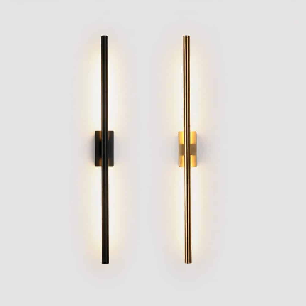 2 tube-shaped wall sconces mounted vertically on a white wall. The sconce on the left is black, the sconce on the right is gold. Light is diffused only through the part of the tube facing the wall.