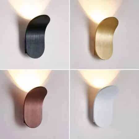 photo divided into 4 with the same modern oval aluminum wall sconce curved upwards lit. Top left is black, top right is gold, bottom left is brown and bottom right is white.