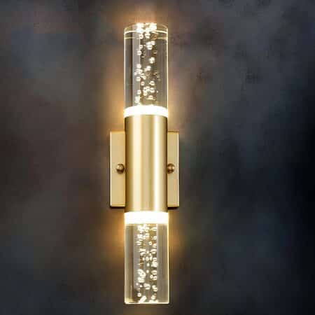 Wall sconce in the shape of a bubble tube with gold support and gold part in the center of the tube. Fixed on a black wall. The wall light is switched on and emits a warm light through the tube.