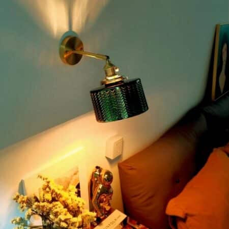 a rustic wall lamp in dark green glass is seen in a living room with a brown sofa