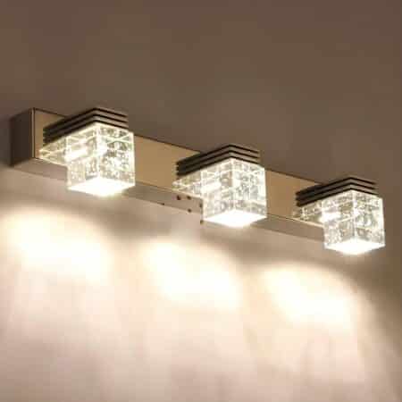 Wall light with rectangular aluminum bracket where 3 acrylic cubes are fixed by an aluminum bar. Light is diffused by the cubes. The wall light is mounted on a beige wall.