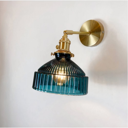 Vintage wall lamp with grooved blue glass shade and gold metal frame. Light bulb on, mounted on a white wall.