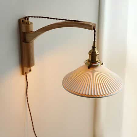 Vintage wall lamp with wooden stand and rotating arm fixed to wooden top. The suspended shade is in white ceramic. The socket is in gilded metal. The cable connecting the socket to the plug runs through the wooden support.
