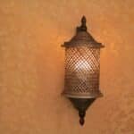 Handcrafted bamboo lantern-style wall lamp mounted on an ochre-colored wall and lit.
