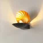 on a light gray background, a black seashell-shaped wall light is lit