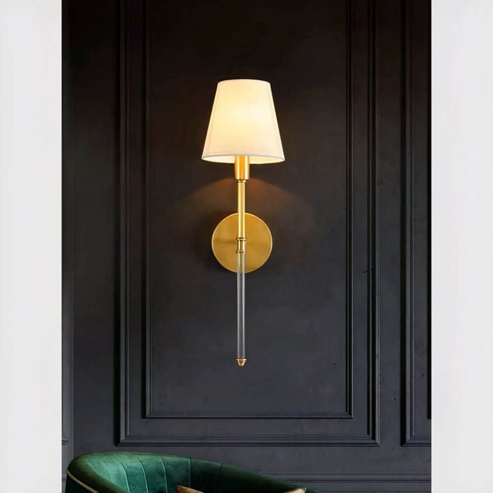 Brass wall light with classic fabric shade, lit and mounted on a gray wall.