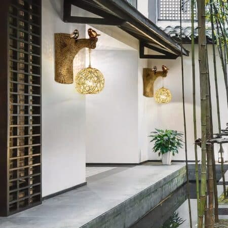 Wicker wall lamp with little birds on a branch, mounted on a white wall and lit.