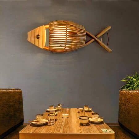Fish-shaped wicker wall light hung on a gray wall above a dining room table set for dinner.