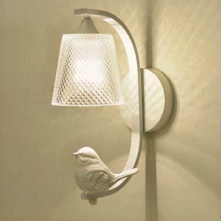 on a beige wall, a glass sconce with a white perched bird is visible