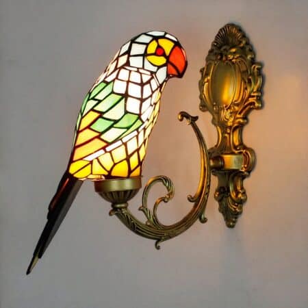 Tiffany-style parrot wall light, in its green version, lit and mounted on a white wall.
