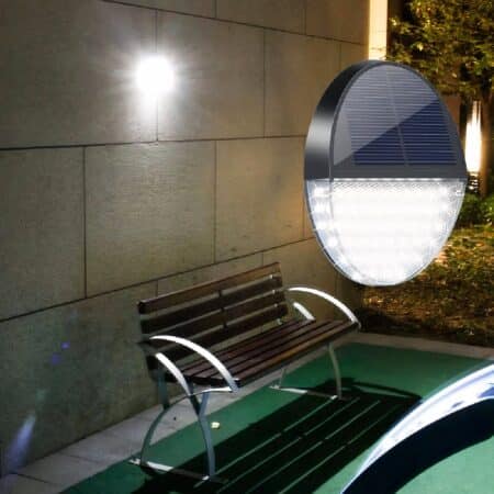 Round solar-powered wall light, lit and mounted on an exterior stone wall, above a bench.