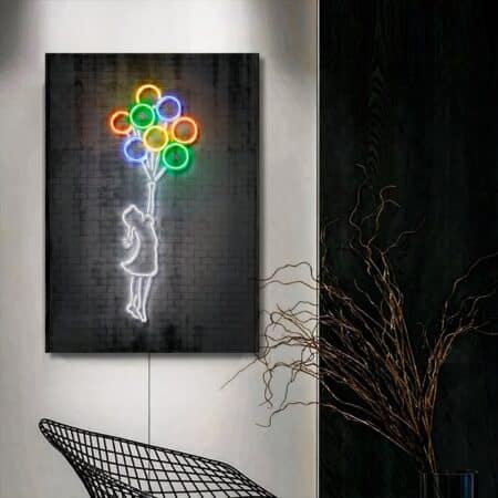 Grey canvas with a motif of a little girl with luminous white outlines holding in her hand balloons whose outlines are luminous and colored. The canvas is on a light gray wall. The right-hand side is black with a branch in front and a metal-style armchair.