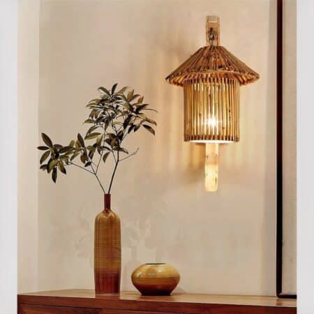 Retro Japanese-style wicker and bamboo wall lamp hanging on a wall above a wooden sideboard with a plant vase.