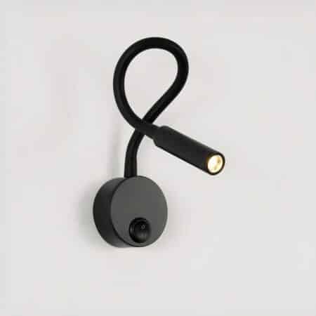 Black wall-mounted reading light, round base with switch, flexible stem and lit LED light head.