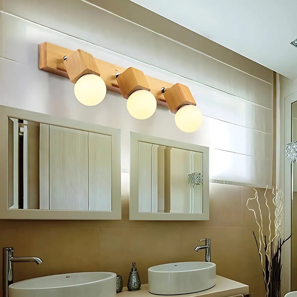Wooden cube-shaped bathroom wall light with 3 light sources. The bulbs are switched on. The wall light is fixed above two rectangular mirrors, themselves above two white washbasins.