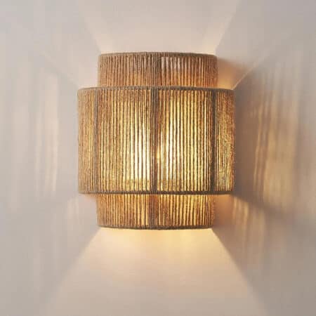 Japandi wall lamp for soothing interiors in beige hand-woven hemp rope illuminated with warm light on a plain background